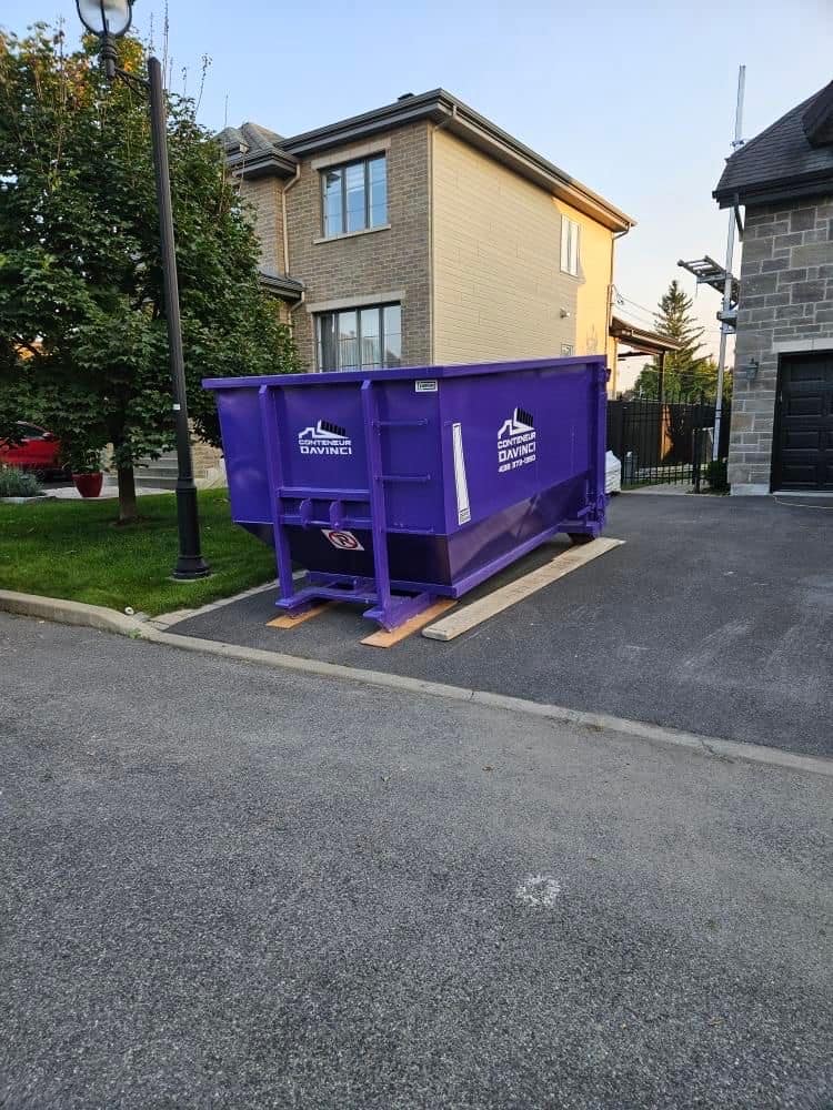 Large purple construction dumpster from Conteneur Davinci placed on a driveway next to a residential house during daytime