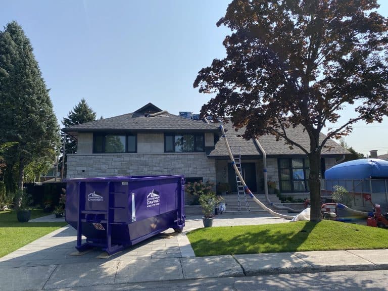 Large two-storey stone house with roof renovation work in progress, including purple Conteneur Davinci dumpster and protective chutes on the roof