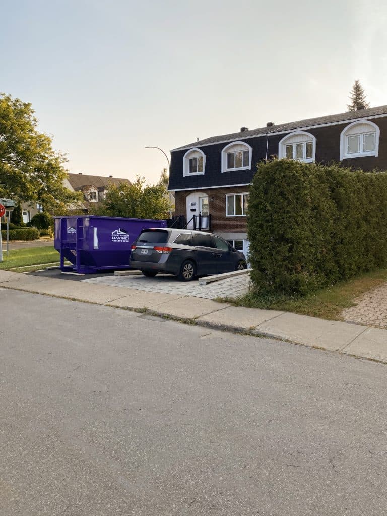 Residential street with a two-storey brick house, a parked minivan, and a large purple rental dumpster