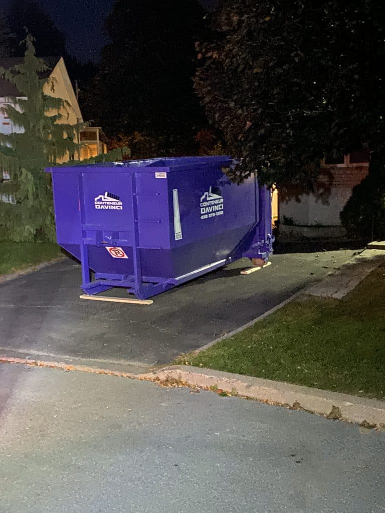 Purple Conteneur Davinci dumpster parked on a residential driveway at night