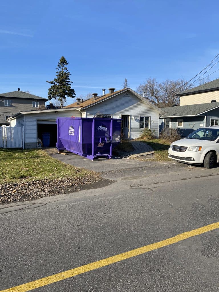 Residential house with a large purple Conteneur Davinci dumpster and a white minivan parked on a sunny day