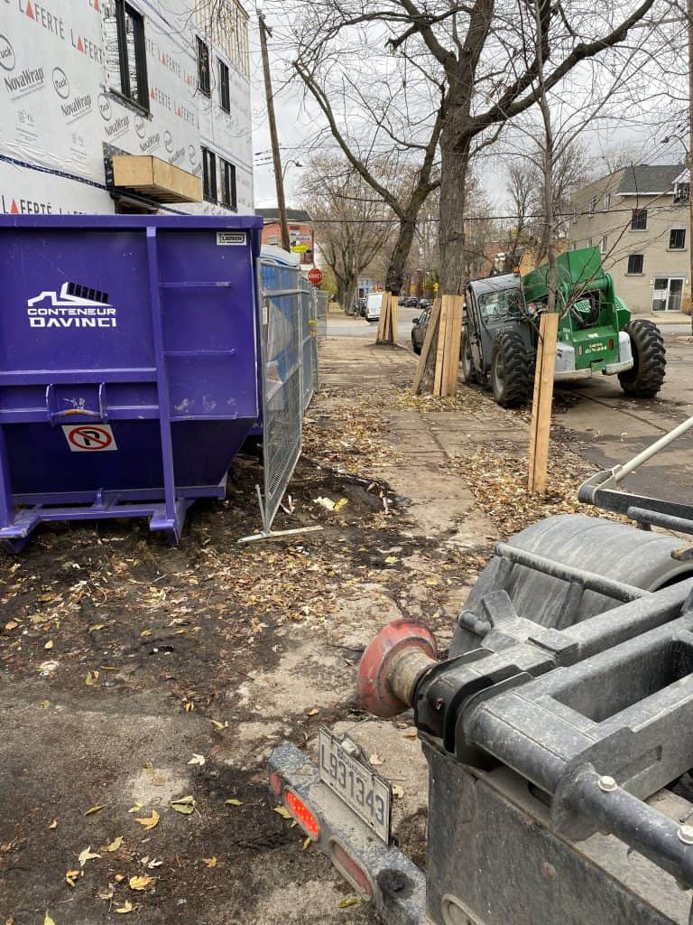 Construction site with a purple dumpster labeled Conteneur Davinci, a green forklift, and a building covered in NovaWrap weather barrier on a cloudy autumn day