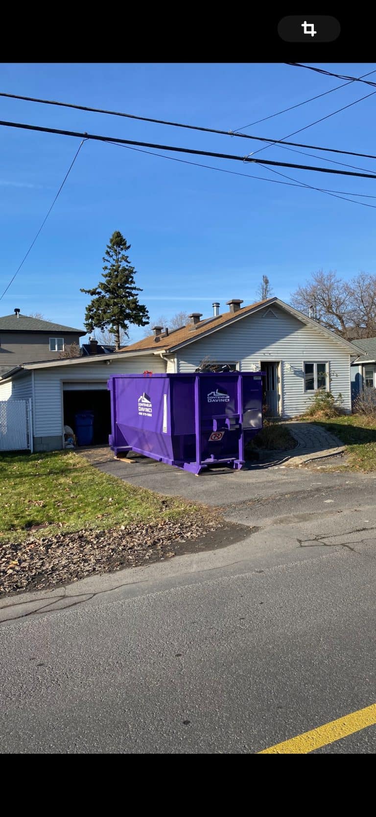 Residential house with a purple Conteneur Davinci dumpster parked in the driveway under clear blue sky
