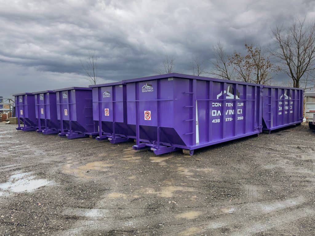 Row of large purple metal dumpsters labeled Conteneur DaVinci on a cloudy day in an outdoor industrial area with bare trees in the background
