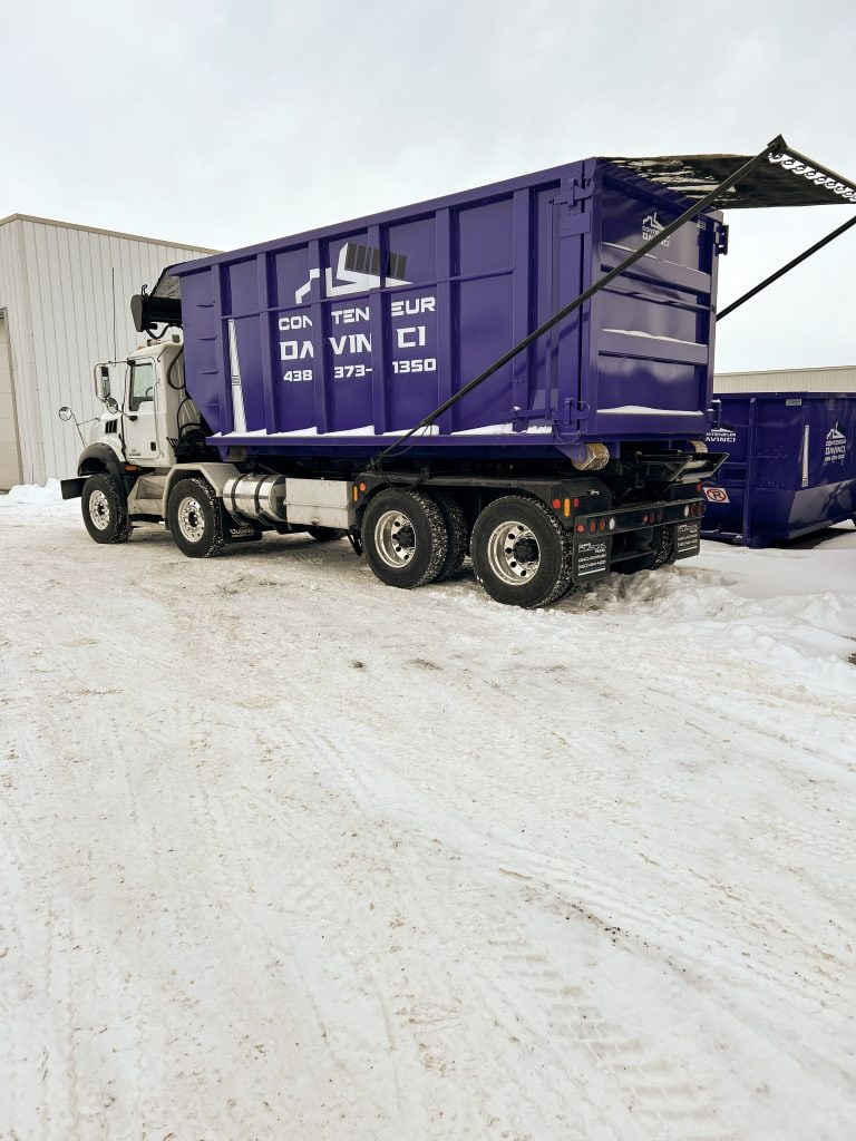 Large white truck with a purple Conteneur Da Vinci container on snowy ground in an industrial area