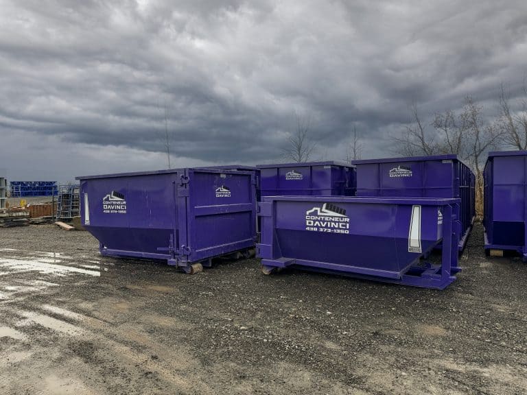 A group of large purple Conteneur DaVinci industrial dumpsters on a gravel lot under an overcast sky
