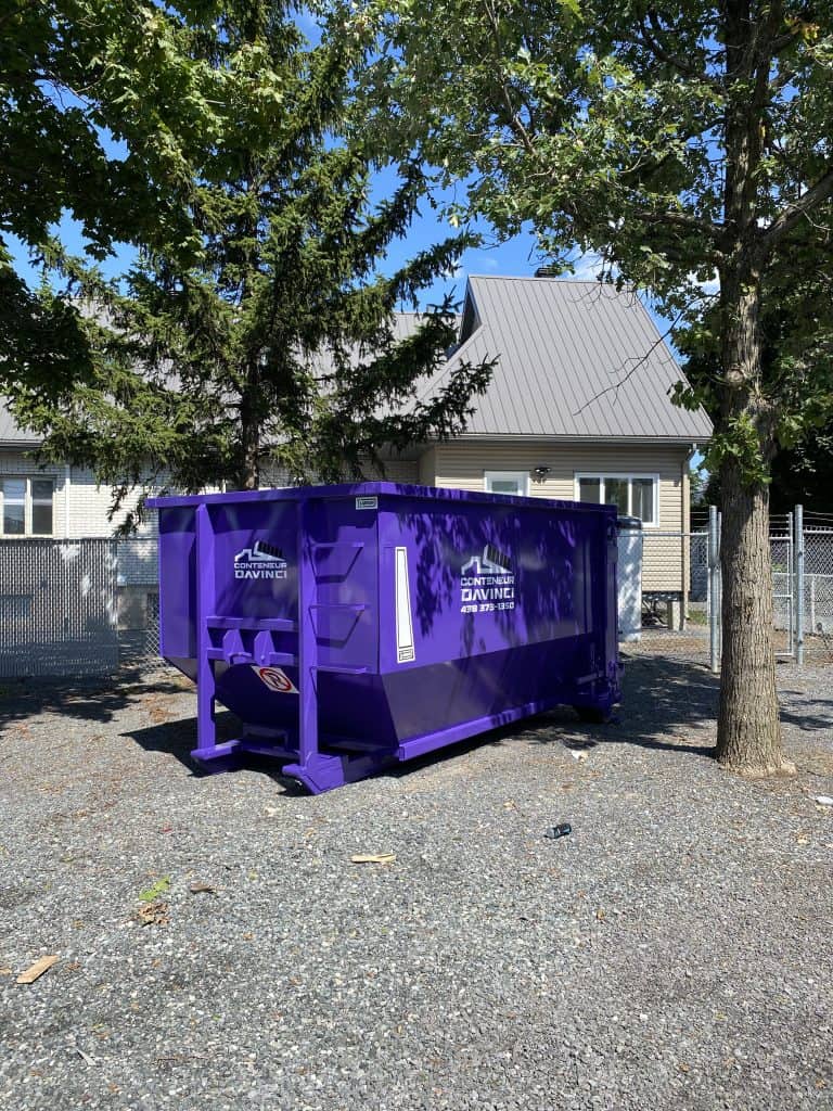 Large purple Conteneur Davinci waste container outside a house surrounded by trees on a sunny day