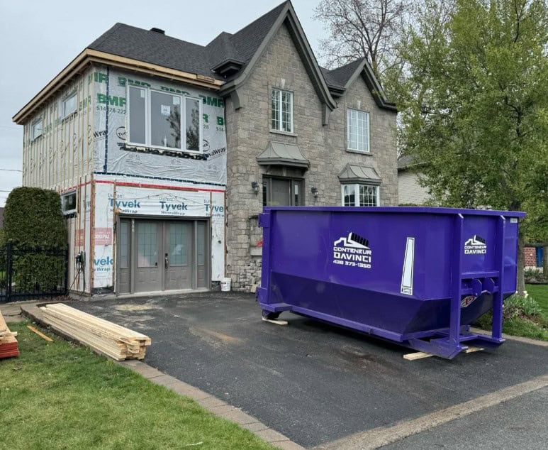 House undergoing exterior renovation with new siding installation and a large purple construction dumpster in the driveway